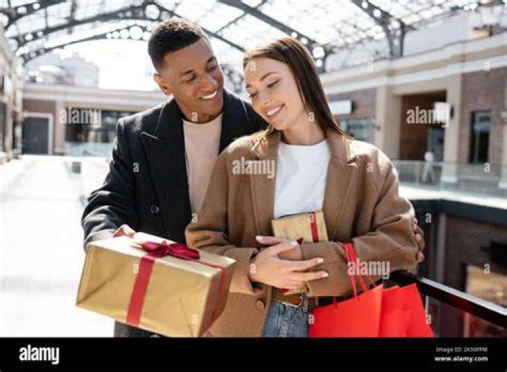 Man with gift near woman on sofa.